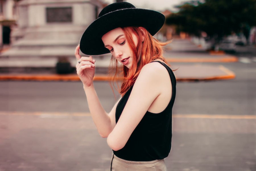 A trans woman with red hair and a black hat posing on a city street in San Antonio.