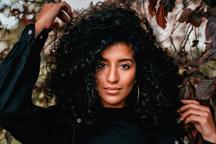 British trans woman looking at the camera, framed by brown and red autumn leaves.