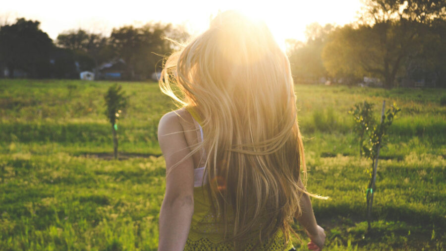 Mujer con cabello largo y rubio caminando por un campo al atardecer.