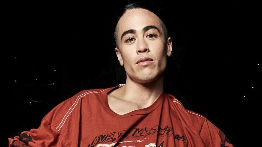 Wu Tsang photographed in a dramatic portrait against a black backdrop, wearing bright red sleeves and nail polish.