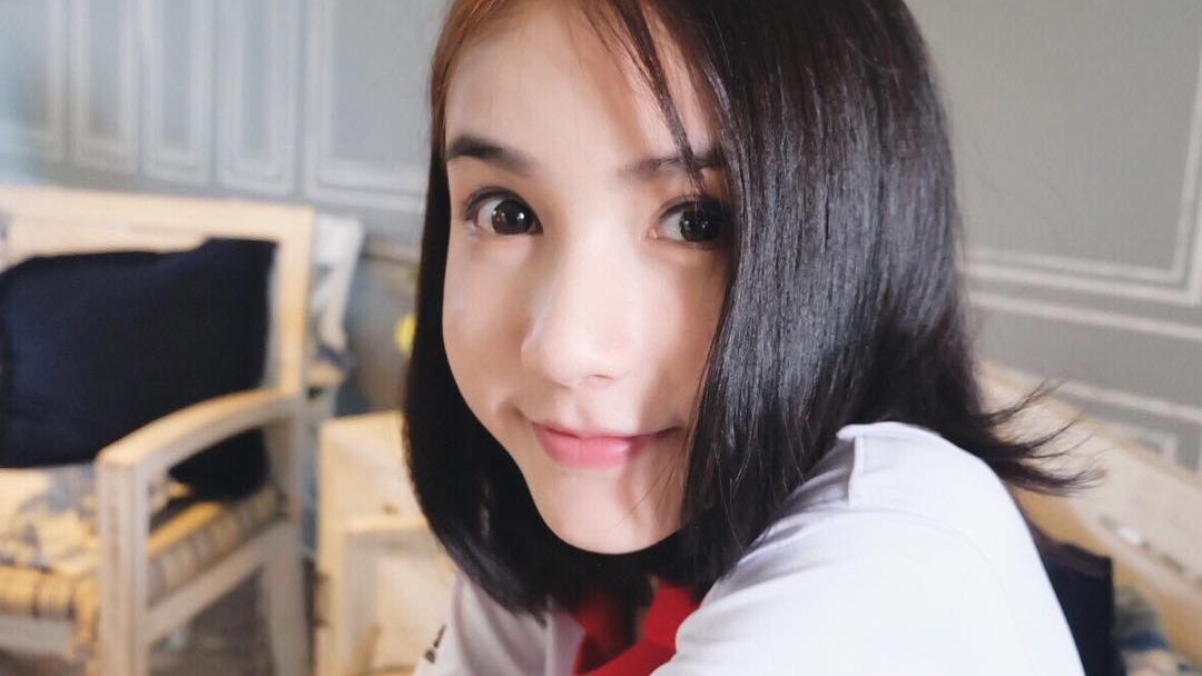 Close-up of a young Yoshi Rinrada smiling softly indoors, wearing a white and red t-shirt.