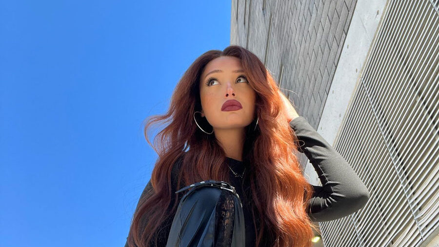 Zoey Luna photographiée en mai 2024, accroupie devant un bâtiment, en cuir noir, avec de longs cheveux roux bouclés.