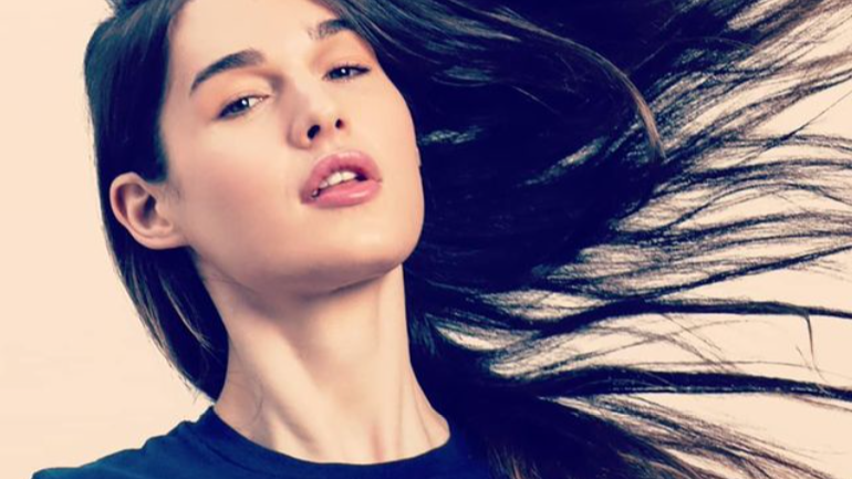 Michelle E. Hendley poses in a navy blue t-shirt with “Equality & Dignity” written in pastel colors, hair flowing to the side.